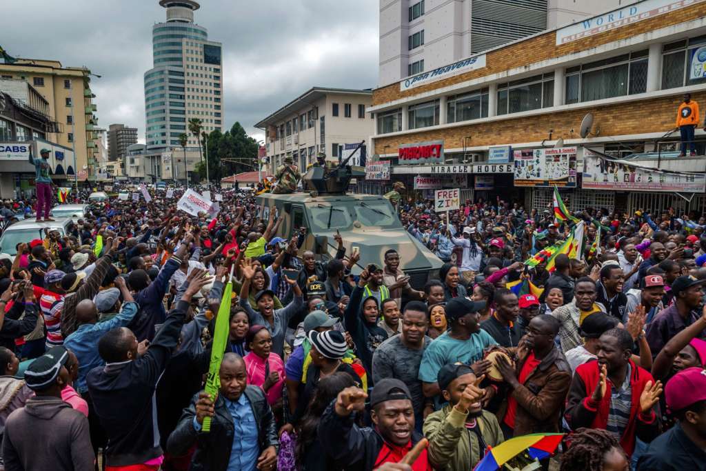 TOPSHOT - People cheer a passing Zimbabwe Defense Force military vehicle during a demonstration demanding the resignation of Zimbabwe's president on November 18, 2017 in Harare. Zimbabwe was set for more political turmoil November 18 with protests planned as veterans of the independence war, activists and ruling party leaders called publicly for Zimbabwe's President to be forced from office. / AFP PHOTO / Jekesai NJIKIZANA (Photo credit should read JEKESAI NJIKIZANA/AFP/Getty Images)